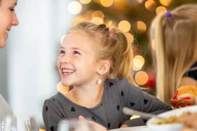 Smilende jente ved festdekket bord under familiejulebord på Gloppen Hotell.